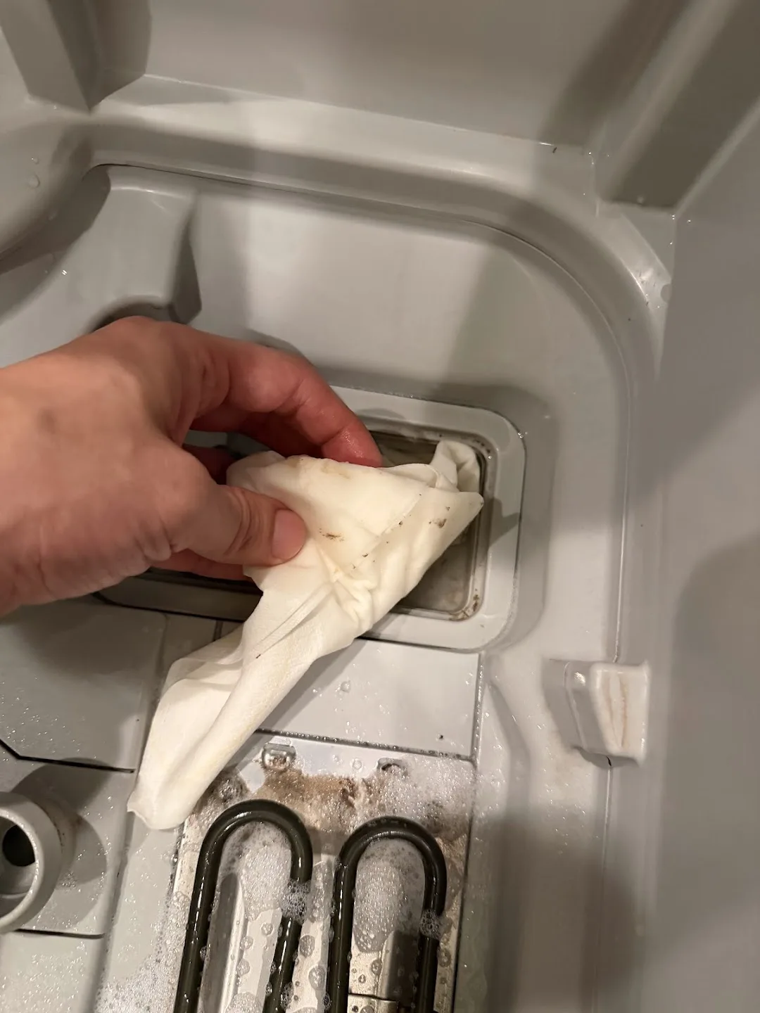 キッチンペーパーで排水トラップのふたのまわりを拭き取っている。紙に茶色い汚れが移っている